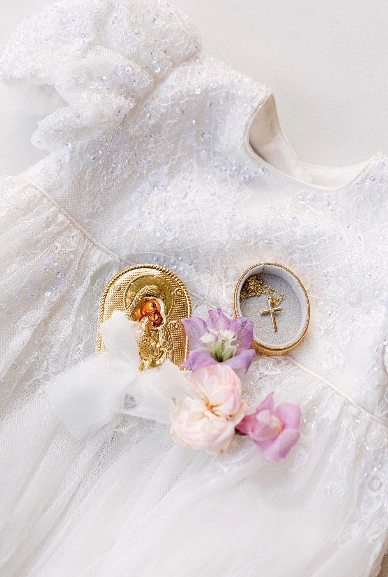 White dress with floral decorations and religious-themed brooches on a white background